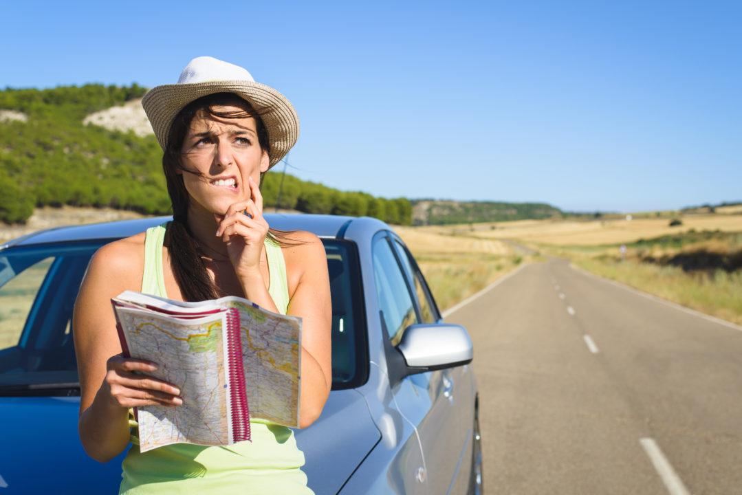 Confused lost woman on car roadtrip travel problem searching in road map.