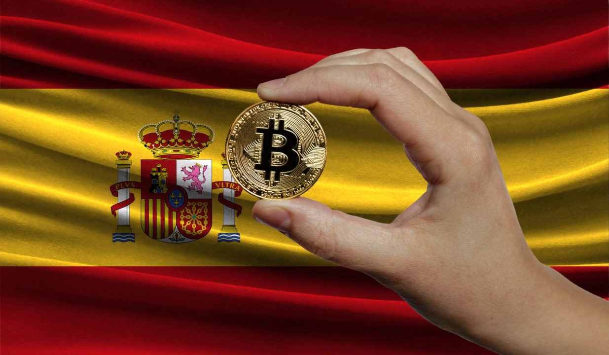 Hand of a man with a gold bitcone Cryptocurrency Digital bit of coins in a hand on a background of the flag of Spain. The concept of virtual money.